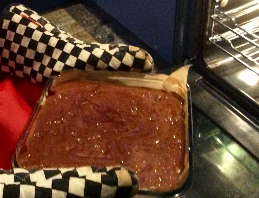 Tray of brownie mix, pair of oven cloves, open oven