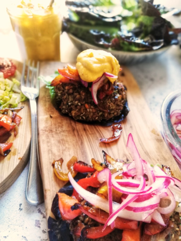 Black bean & freekeh burger with trimmings,on wooden board, pickled onions, butternut squash dressing.