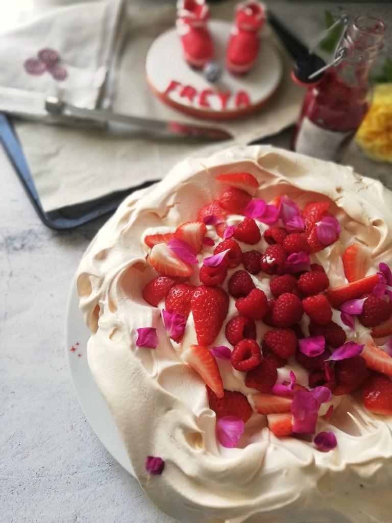 Strawberry and raspberry pavlova, with rose petals, berry coulis